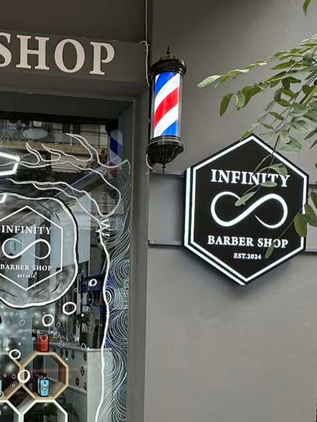 Η πρόσοψη του Infinity Barber Shop στην Κωνσταντινουπόλεως 41: το φωτιζόμενο εξαγωνικό σήμα INFINITY BARBER SHOP EST.2024, η κλασική κολόνα κουρείου και η χαραγμένη τζαμαρία